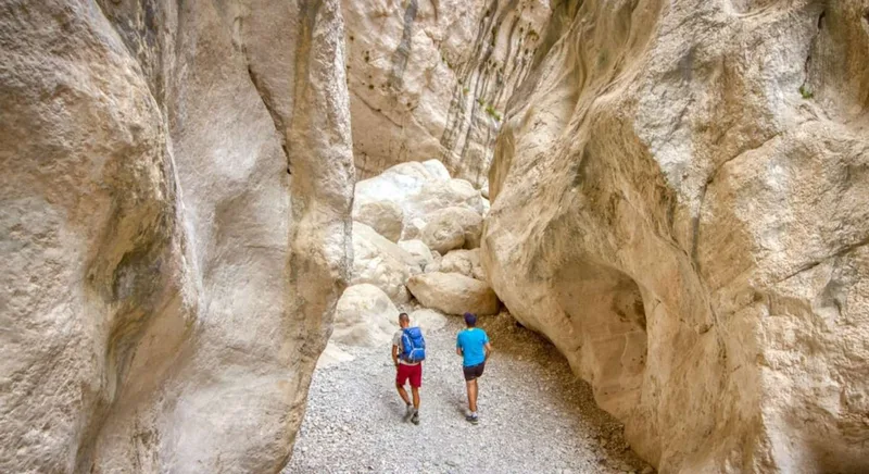 Two hikers walking between the towering pale limestone walls of the Gorropu canyon on a guided sardinia hiking tour from Orosei or Dorgali in the Supramonte